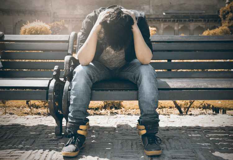 man in black shirt and gray denim pants sitting on gray padded bench